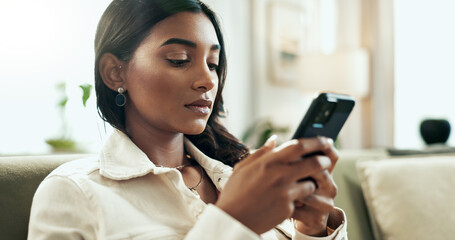 Poster - App, phone and serious Indian woman on sofa in living room of home for communication or research. Internet, social media and text message with person typing on mobile in apartment for networking