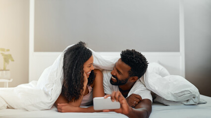 Canvas Print - Selfie, bedroom and couple with smile, love and relax with comfort, bonding together and memory. House, mobile user and man with woman, happiness and joy with weekend break, morning and relationship