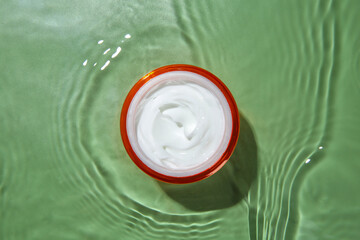 Poster - Jar with cream in water on light green background, top view. Cosmetic product