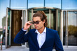 © Alex Vog - Portrait of young businessman in blue suit holding sunglasses in business district, confident looking side away. Serious male near building corporate company in financial district. Copy ad text space