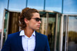 © Alex Vog - Portrait of perfect businessman in blue suit and sunglasses in business district, serious looking side away. Confident male near building corporate company in financial district. Copy ad text space