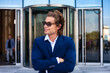 © Alex Vog - Portrait of smiling young businessman in blue suit arms crossed in business area, positive looking side away. Business male near building corporate company in financial district. Copy ad text space
