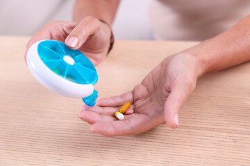 Wall Mural - Senior woman pouring pills from organizer into hand at table indoors, closeup