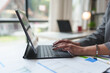 © Phimwilai - Female office worker using hands to type business data on laptop, tablet placed on desk in modern office atmosphere. Concept of working online, expertise, working idea.