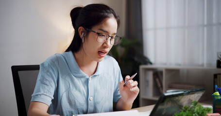 Portrait of Female freelancer sitting at desk wear wireless headphones having video call to explain work to coworkers via digital tablet in home office. Working from home