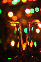 Two transparent wine glasses filled with water, with colorful Christmas lights on a tree in the background