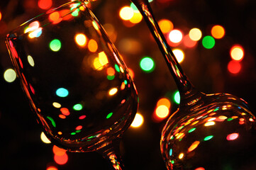 Two transparent wine glasses filled with water, with colorful Christmas lights on a tree in the background