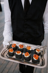 Elegant waiter serving gourmet appetizers on tray at formal outdoor evening event concept