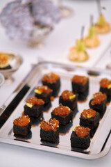 Gourmet black sushi squares topped with vibrant caviar served at a luxury event concept