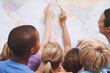 © STEEXBuyout/peopleimages.com - World map, teacher and students with education, back and conversation with creativity. Geography, support and kids in school, children or studying with answers, friends and learning with earth poster
