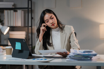 Late Night Focus: A determined businesswoman meticulously reviews documents at her desk, illuminated by a warm desk lamp. The image captures the quiet dedication of a night worker, highlighting the co