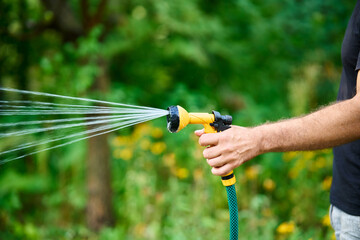 Cropped image of young man watering flowers and plants in garden