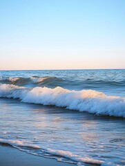 Wall Mural - A wave breaks on the shore at sunset, creating a foamy white crest against the clear blue water and the pale pink sky.