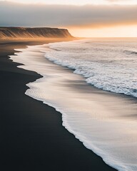 Wall Mural - A serene black sand beach at sunset with gentle waves lapping at the shore, creating a beautiful contrast of colors.