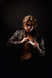© Alex Vog - Perfect young man in unbuttoned image leather jacket showing visit card posing in black studio shadow, looking at camera. Handsome guy fashion model with lovely muscular sexy torso. Copy ad text space
