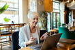 © Davor - Senior businesswoman having video call on laptop in cafe