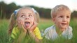 © maxximmm - little girl showing her tongue to her brother lying on the grass in the park. happy family kid dream concept. small children play in fun the summer in nature in the park in the green grass