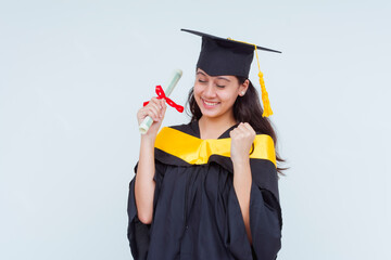 A smiling female graduate in cap and gown celebrating while holding her diploma. Bachelor of Science graduate, isolated on a white background.