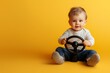 © Bundi - An adorable little baby sitting in a denim outfit, holding a steering wheel, and smiling with pure joy against a yellow studio background. A concept of childhood, parenthood, care, and education.