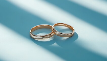 Wall Mural - Two gold wedding rings on a blue surface with shadow.