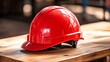 © Naphol - A vibrant red hard hat resting on a wooden surface, symbolizing safety and protection in construction and industrial environments.