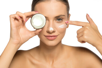 Beautiful young woman holding a jar of face cream in her hand as she applies it to her skin