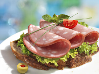 Sandwich with boiled sausages and lettuce leaves in white plate  on blurred background