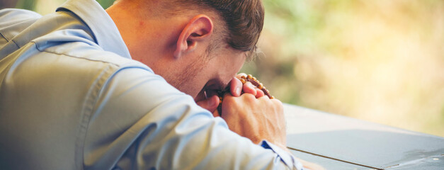 Pray and bible concept. Hand in hand together on bible by Caucasian man (worship christian), thinking and closed her eyes at church. Person side view, male praying, hope for peace-vertical image.