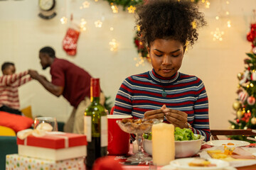 A joyful family gathers around the dinner table celebrating Christmas. The father, dressed in a Santa hat, gives a gift to the child, while everyone smiles with warmth and festive decorations.