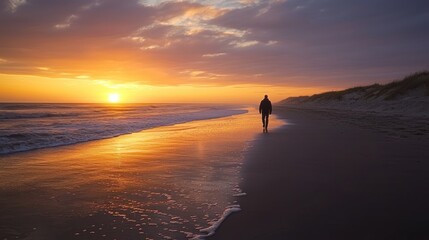 Wall Mural - A man walking by himself on a deserted beach at sunset.