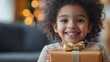 © Wendelin - A child smiling while looking straight ahead, holding a gift box in their arms, happy