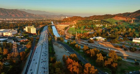 Wall Mural - Footage above the multi-lane highway with lively traffic at sunset. Urban landscape of Los Angeles, California crossed by the river.