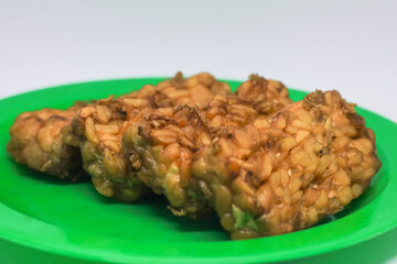 Fried tempeh food is served on a small green plate with a white background