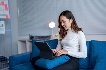 Wall Mural - young asian businesswoman sitting on sofa and using digital tablet with keyboard