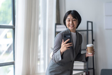 Wall Mural - Businesswoman holding coffee and using smartphone in modern office