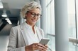© useful pictures - A middle-aged woman with stylish glasses smiles as she interacts with her smartphone in a bright and contemporary office environment, illuminated by natural light