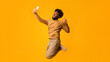 © Prostock-studio - Selfie lover. Black emotional man taking selfie in the air, showing peace gesture, orange background