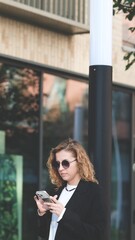 Caucasian woman with curly hair using her mobile phone outdoors. Close-up. Communication technology and modern lifestyle concept