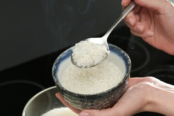 Wall Mural - Woman taking boiled rice from pot into bowl, closeup