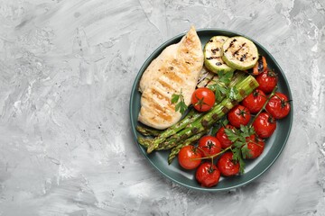 Delicious grilled vegetables and chicken breast on light grey textured table, top view. Space for text