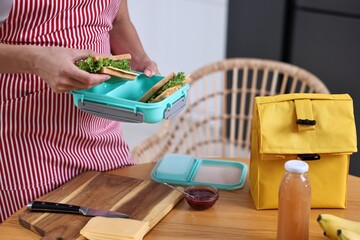 Wall Mural - Woman packing school lunch box with healthy snacks at table in kitchen, closeup