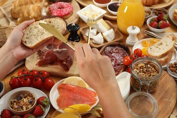 Wall Mural - Woman eating different food during brunch at wooden table, closeup