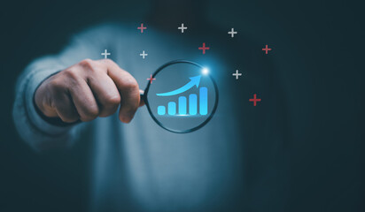 Trader holding magnifier glass with bar graph with increasing arrow of stock market chart. Business finance and investment concept. Developing potential with marketing strategy for business growth.