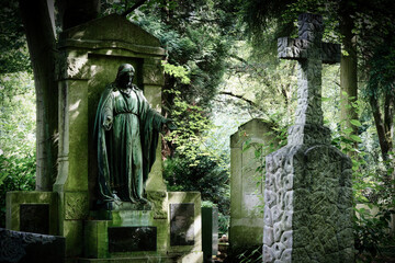 Ancient gravestones in the semi-darkness of the old trees of the famous historic Melaten cemetery in Cologne