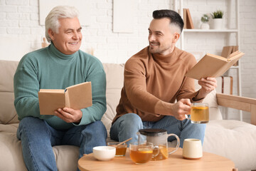 Wall Mural - Young man with his father drinking lemon tea and reading books at home