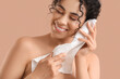 © Pixel-Shot - Young African-American woman removing makeup with towel on beige background, closeup