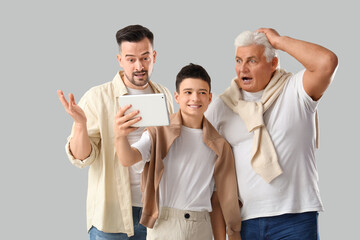 Poster - Teenage boy with his dad and grandfather using tablet computer on light background