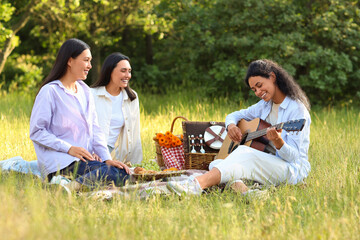 Wall Mural - Female friends playing guitar on picnic in park