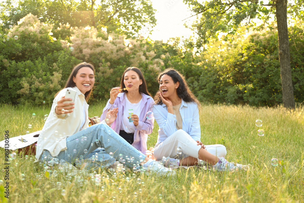 Young women with soap bubbles taking selfie on picnic in park