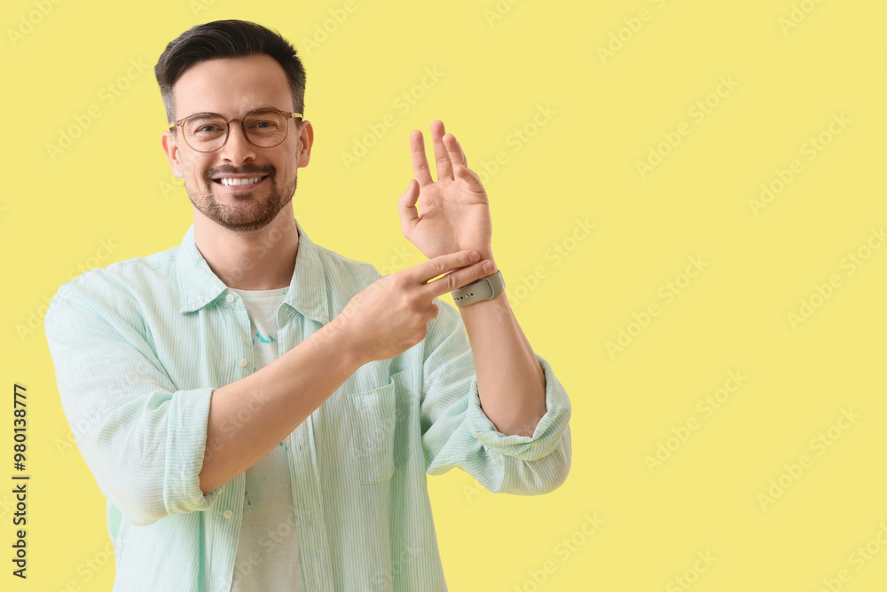 Young man checking his pulse on yellow background